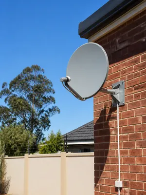 Satellite dish wall-mounted on a face-brick home with the cable run neatly down to a wall gland