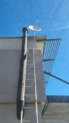 Satellite dish being fitted at roof level with a ladder up against the wall