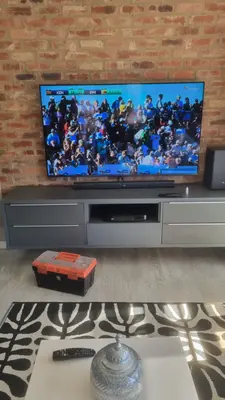 TV on a wall mount with soundbar and decoder, set up for watching the sport